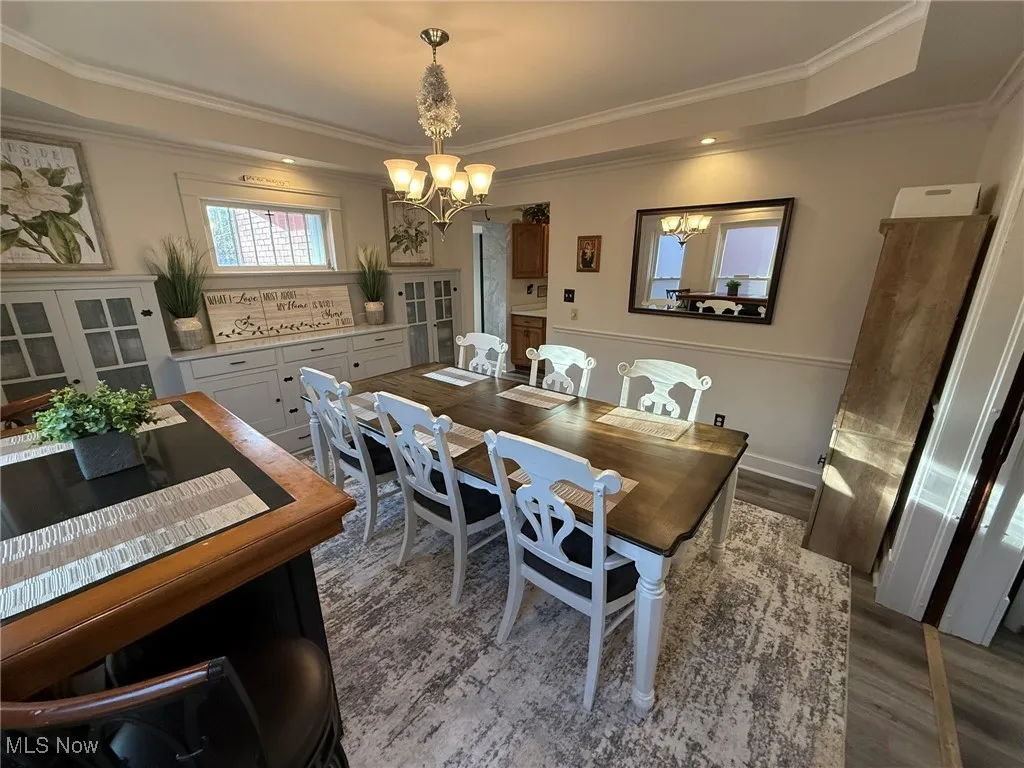 Dining space with a raised ceiling, crown molding, wood finished floors, and a chandelier