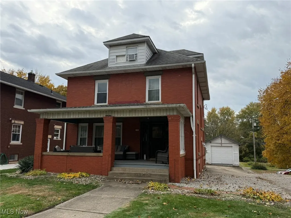 Traditional style home with a porch, brick siding, an outbuilding, and a front yard
