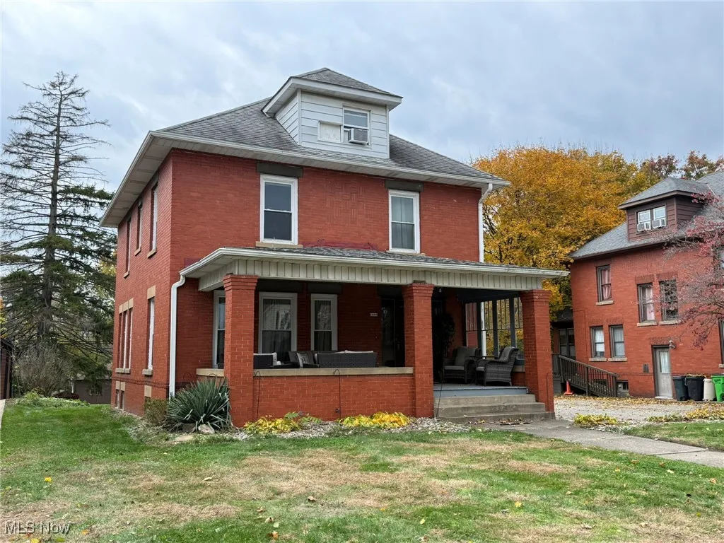 American foursquare style home featuring brick siding, a front lawn, and covered porch