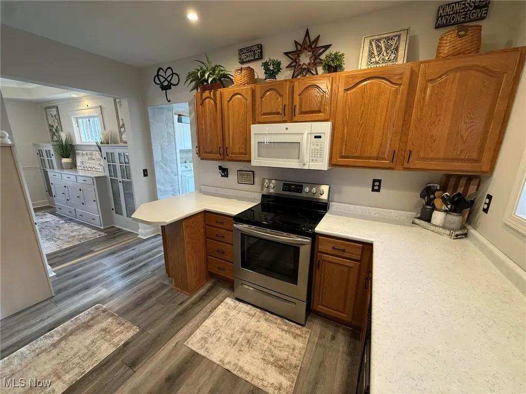 Kitchen with electric stove, light countertops, brown cabinets, white microwave, and recessed lighting