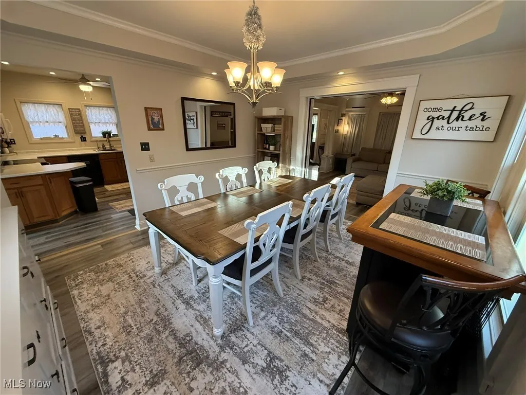 Dining area featuring ornamental molding, dark wood-style floors, a chandelier, a tray ceiling, and ceiling fan