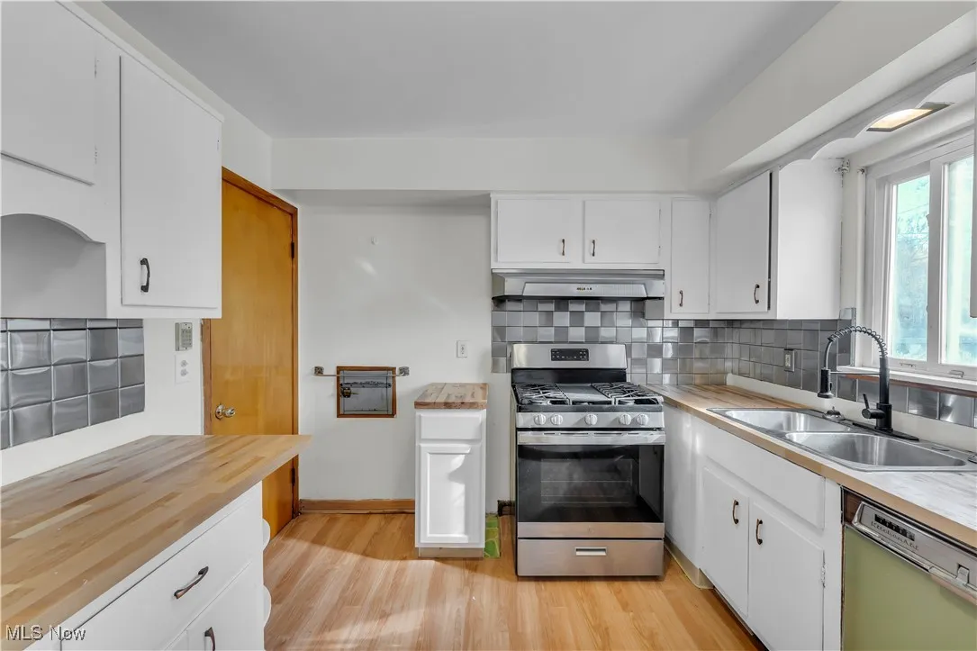 Kitchen featuring white cabinetry, stainless steel range with gas stovetop, light wood finished floors, backsplash, and under cabinet range hood