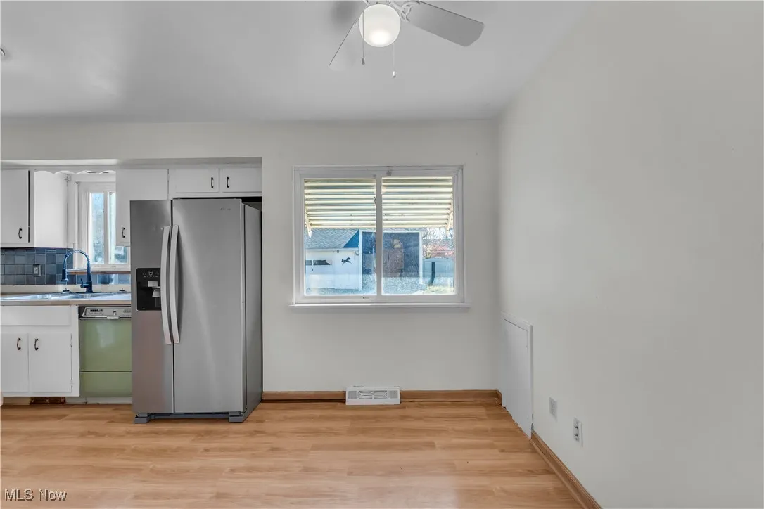 Kitchen featuring stainless steel fridge, white cabinets, light countertops, and light wood finished floors