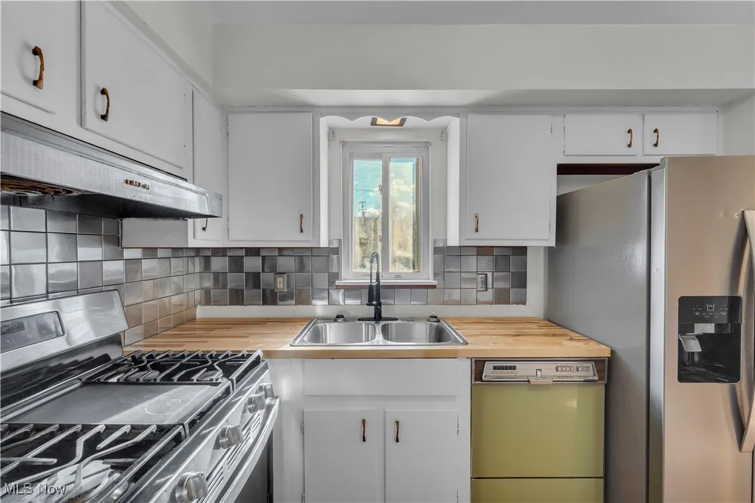 Kitchen featuring stainless steel appliances, white cabinets, backsplash, and under cabinet range hood