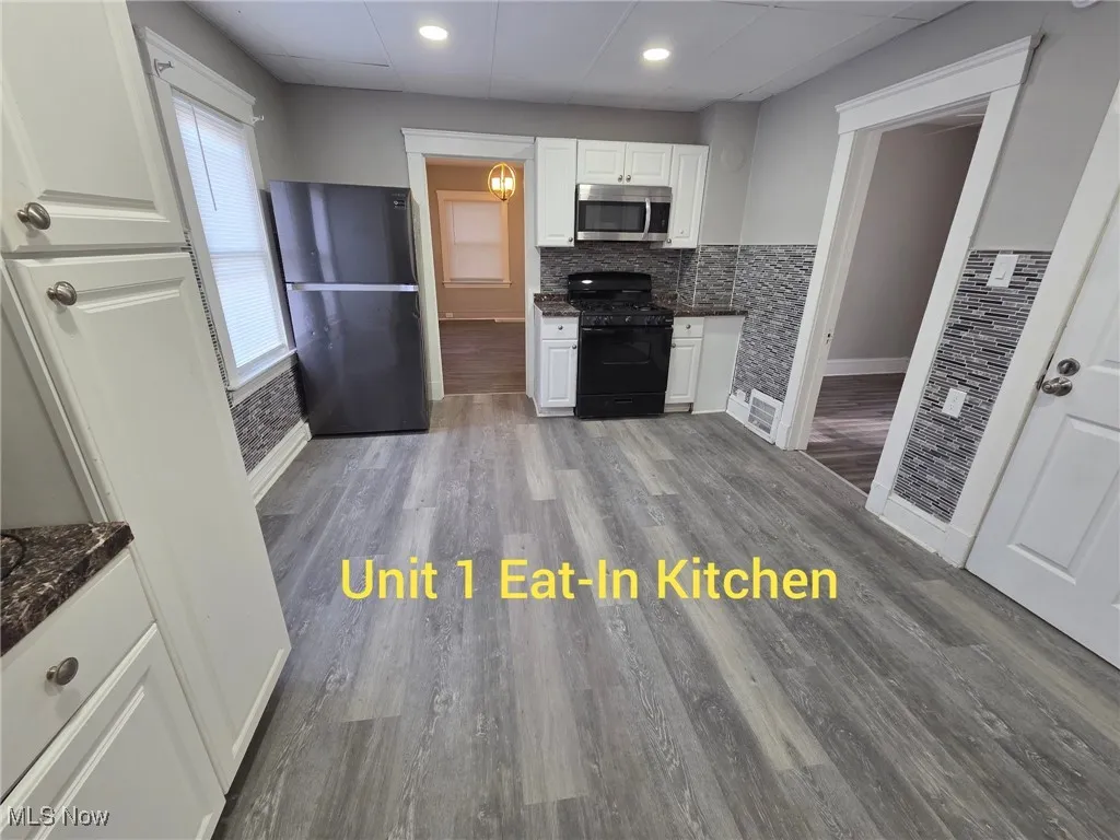 Kitchen featuring dark wood finished floors, white cabinetry, black appliances, recessed lighting, and dark stone countertops