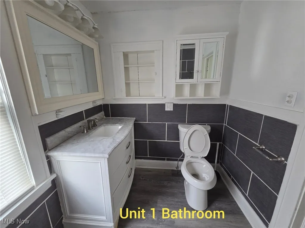 Half bathroom featuring tile walls, vanity, dark wood-style flooring, and a wainscoted wall