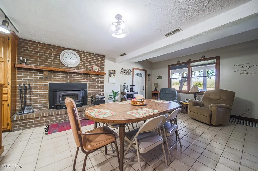 Dining area featuring light tile patterned floors, a brick fireplace, beamed ceiling, and a textured ceiling