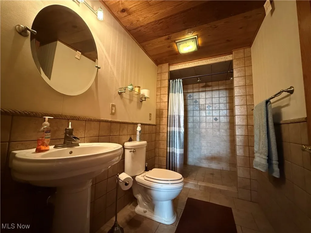 Full bathroom featuring wooden ceiling, a shower stall, tile walls, and wainscoting