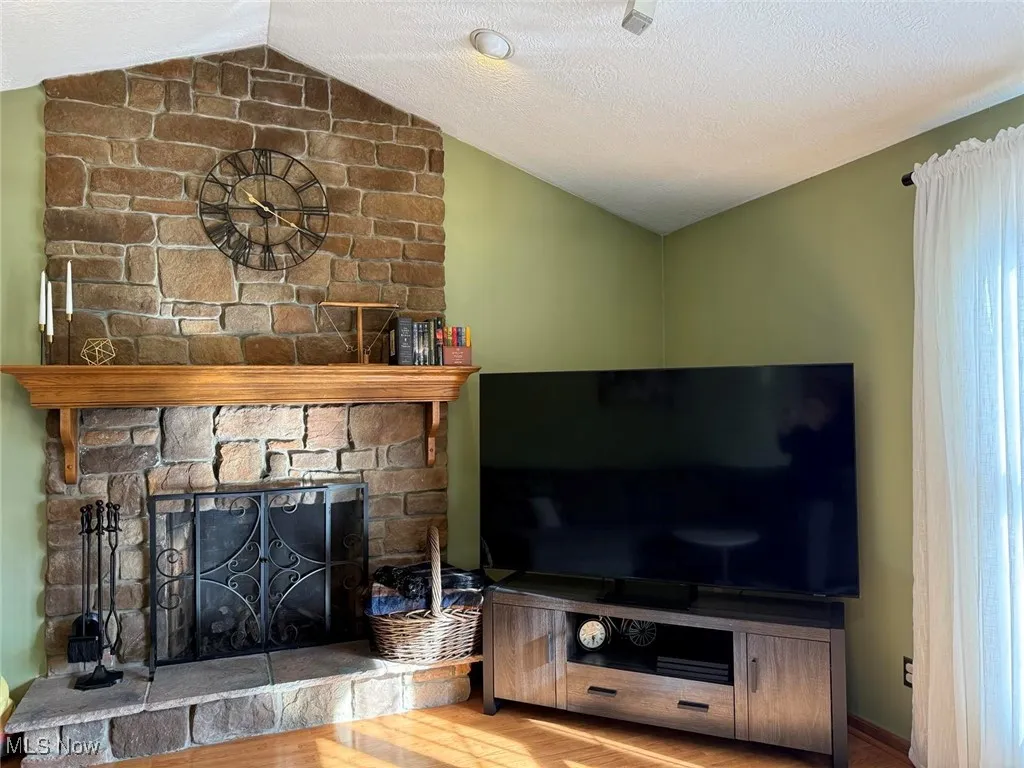 Unfurnished living room with lofted ceiling, a stone fireplace, a textured ceiling, and wood finished floors
