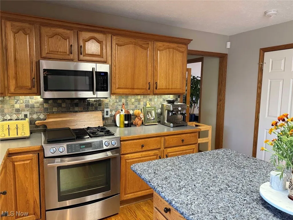 Kitchen featuring stainless steel appliances, tasteful backsplash, brown cabinets, and light wood-style flooring
