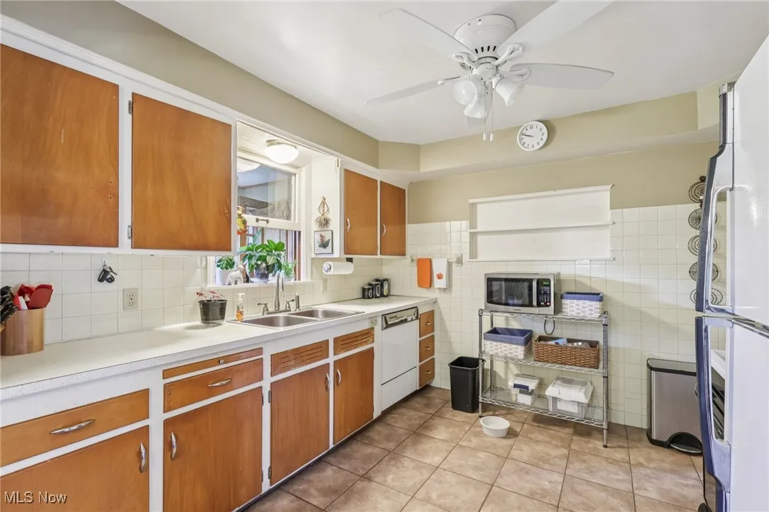 Kitchen with light countertops, light tile patterned flooring, white appliances, brown cabinetry, and decorative backsplash