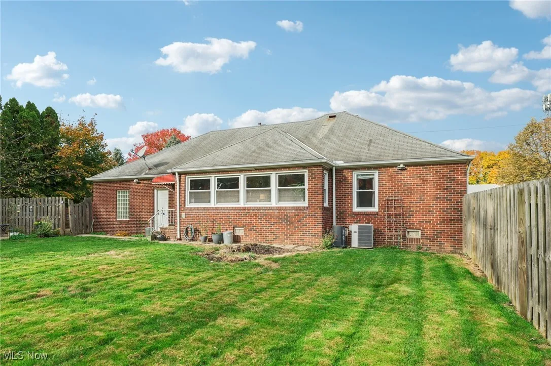 Back of property with a fenced backyard, brick siding, and roof with shingles