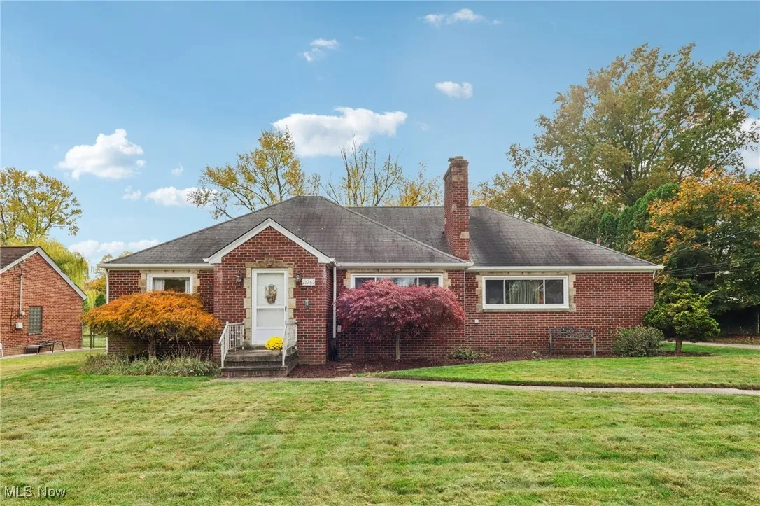 View of front facade featuring a front lawn, a chimney, brick siding, and roof with shingles