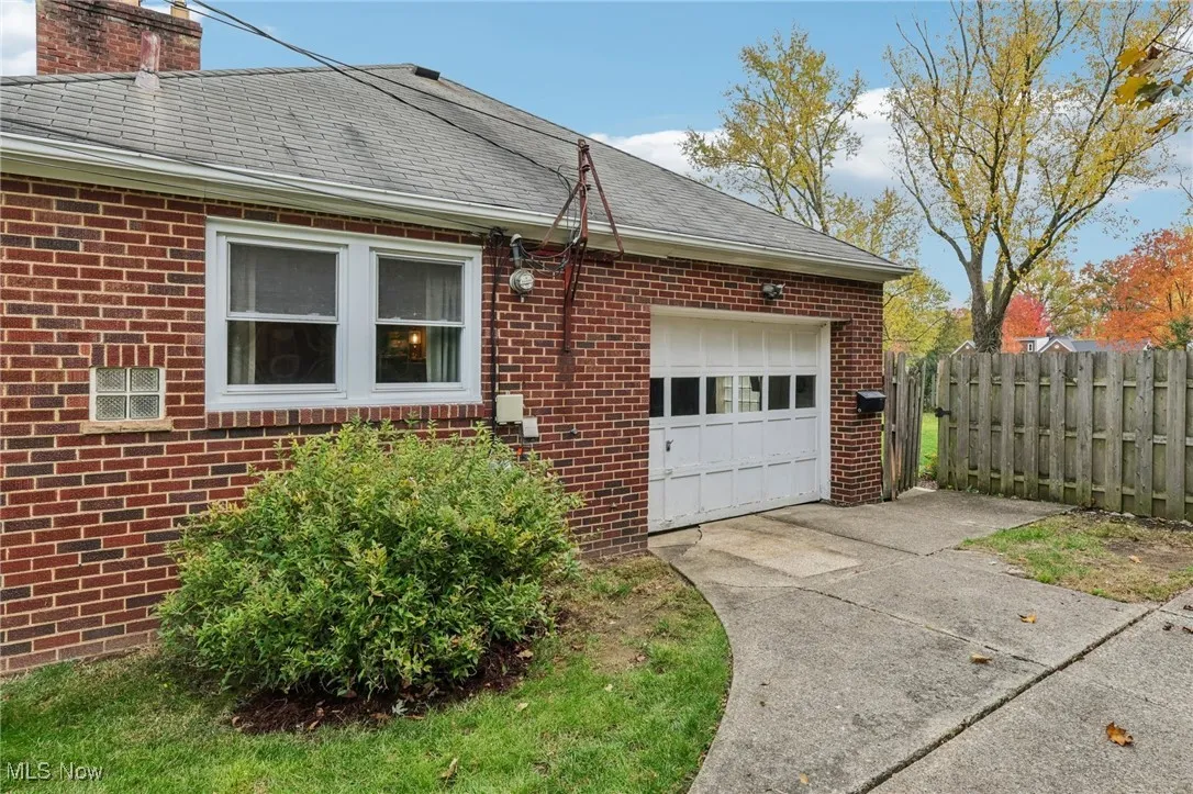 View of side of home featuring a shingled roof, a garage, brick siding, driveway, and a chimney
