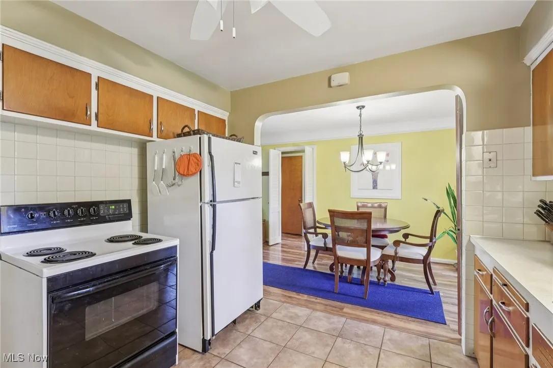 Kitchen featuring decorative backsplash, electric range oven, light countertops, brown cabinetry, and light tile patterned floors