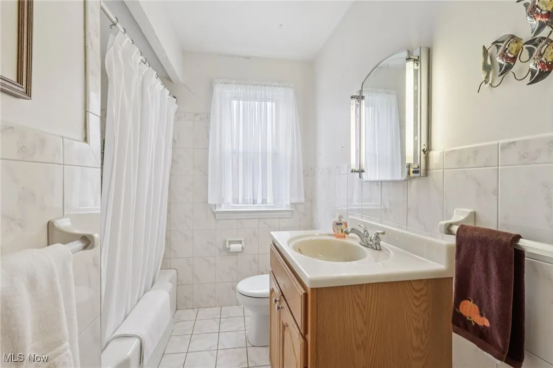 Bathroom with tile walls, vanity, light tile patterned floors, shower / bath combo with shower curtain, and a wainscoted wall