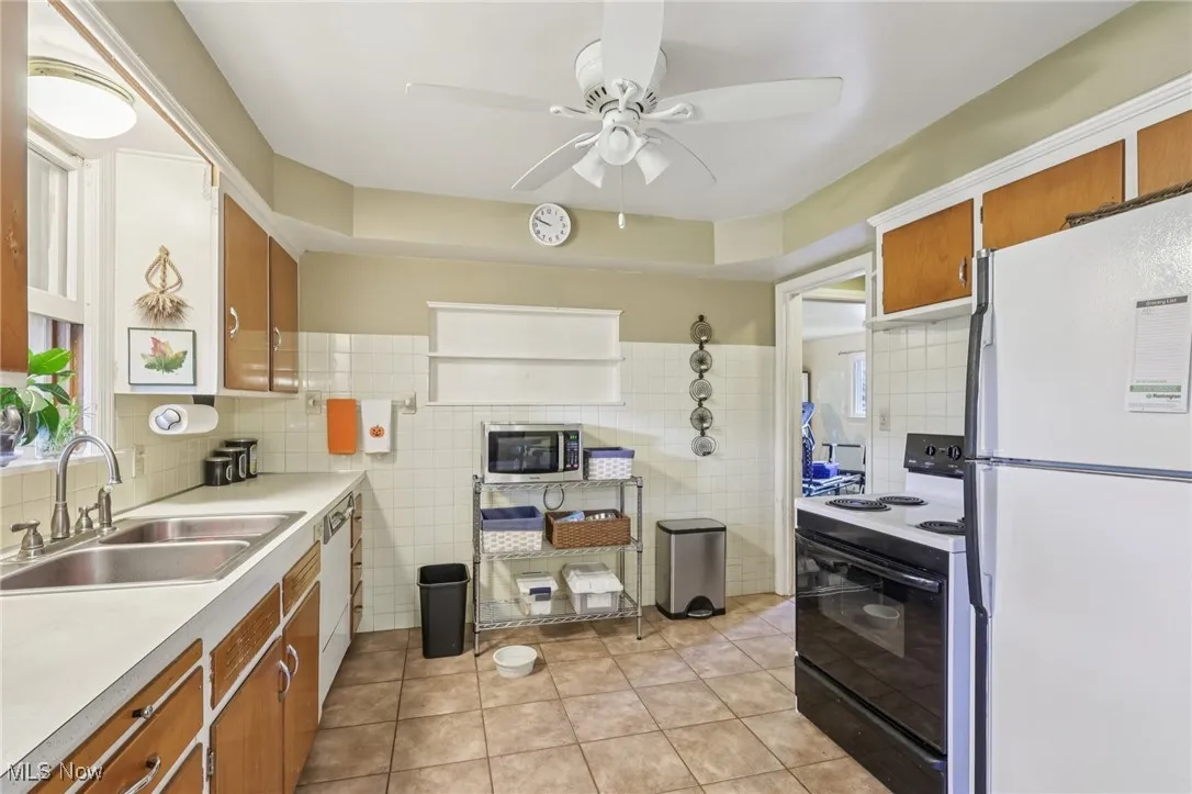 Kitchen with brown cabinets, white appliances, light tile patterned floors, light countertops, and tile walls