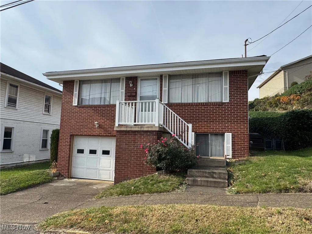 View of front facade with brick siding, driveway, an attached garage, a balcony, and a front yard