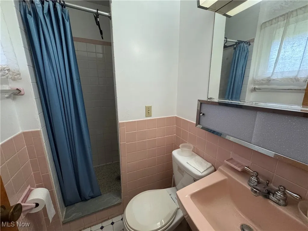 Full bathroom with tile walls, a shower stall, a wainscoted wall, and tile patterned floors