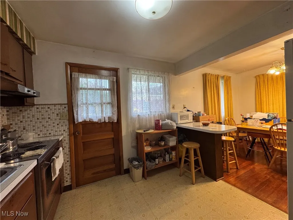 Kitchen featuring a peninsula, light floors, a breakfast bar, light countertops, and stainless steel electric range