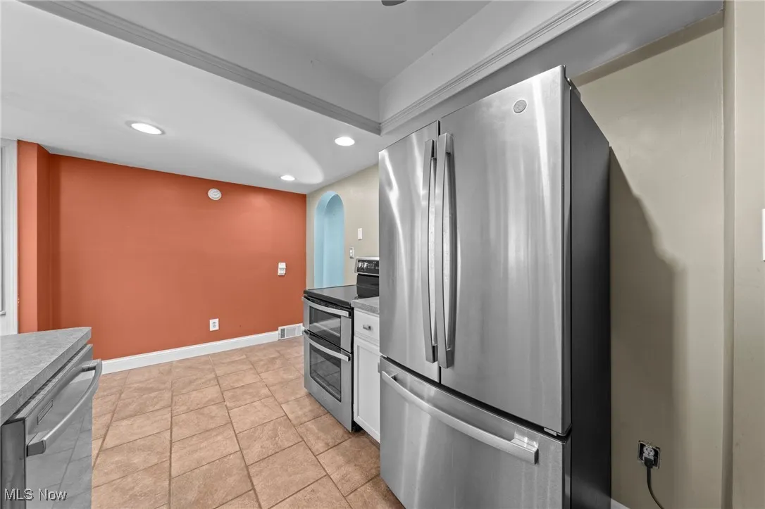 Kitchen featuring appliances with stainless steel finishes, recessed lighting, white cabinets, arched walkways, and light tile patterned flooring