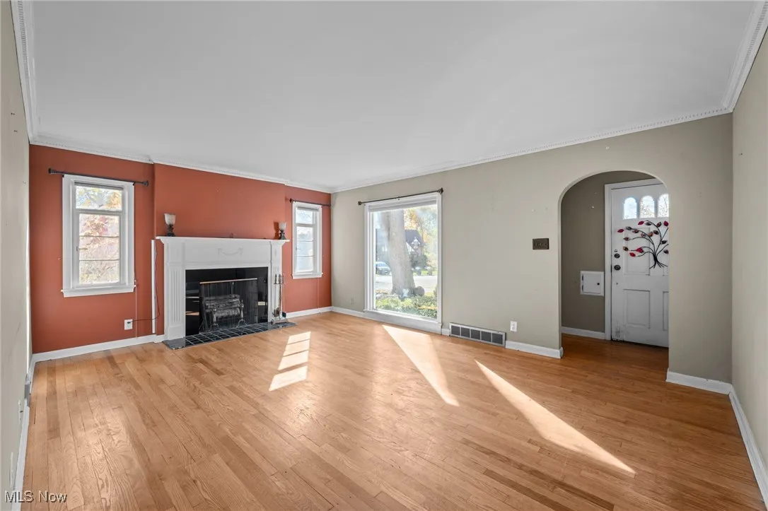 Unfurnished living room with ornamental molding, light wood-style flooring, a fireplace with flush hearth, plenty of natural light, and arched walkways