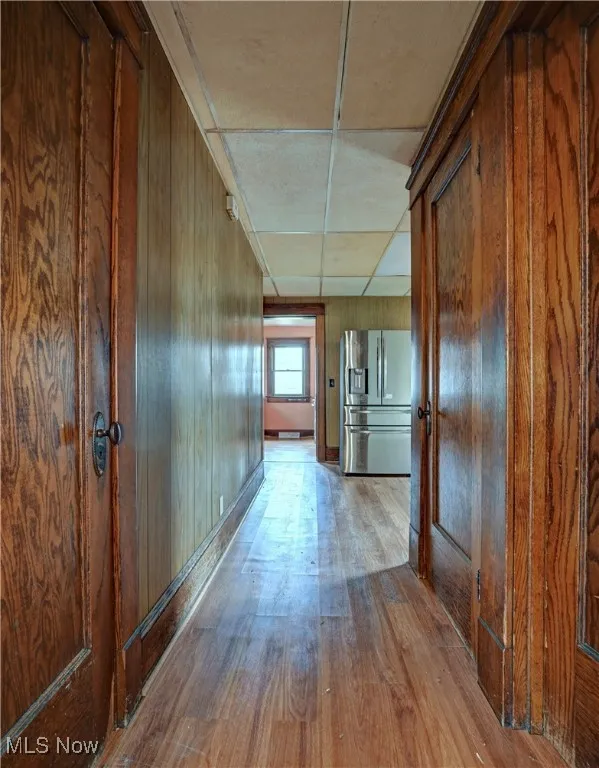 Corridor with wood-type flooring, wooden walls, and a drop ceiling