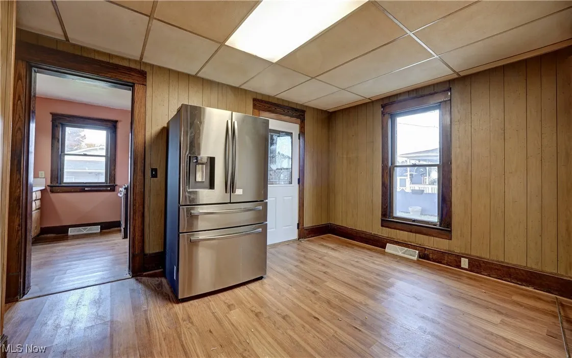 Kitchen featuring wooden walls, stainless steel fridge, plenty of natural light, a drop ceiling, and light wood-style flooring