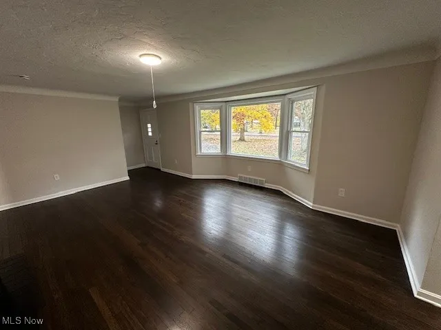 Unfurnished room with a textured ceiling, dark wood-type flooring, and ornamental molding
