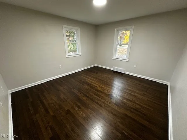 Spare room with dark wood-style flooring and baseboards