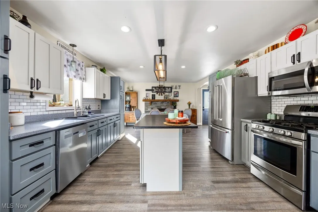 Kitchen with backsplash, stainless steel appliances, hanging light fixtures, white cabinetry, and dark wood finished floors