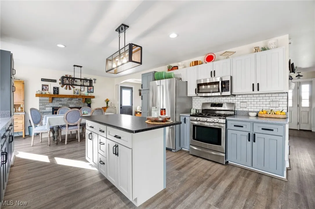 Kitchen with white cabinetry, arched walkways, stainless steel appliances, backsplash, and dark countertops