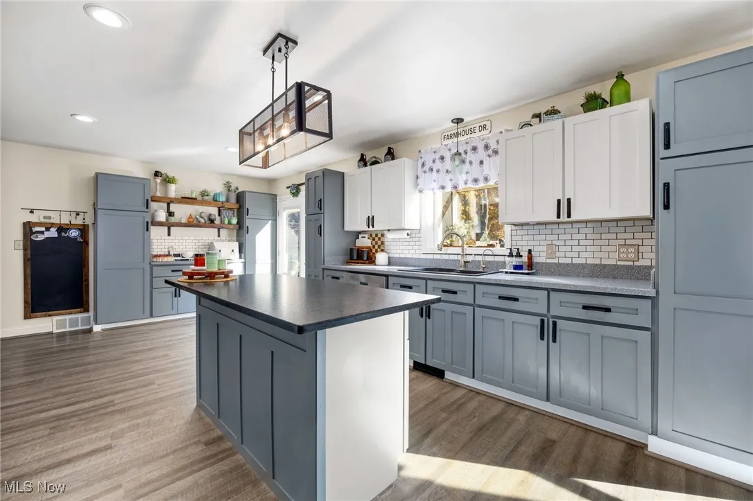 Kitchen featuring gray cabinets, dark countertops, open shelves, tasteful backsplash, and pendant lighting