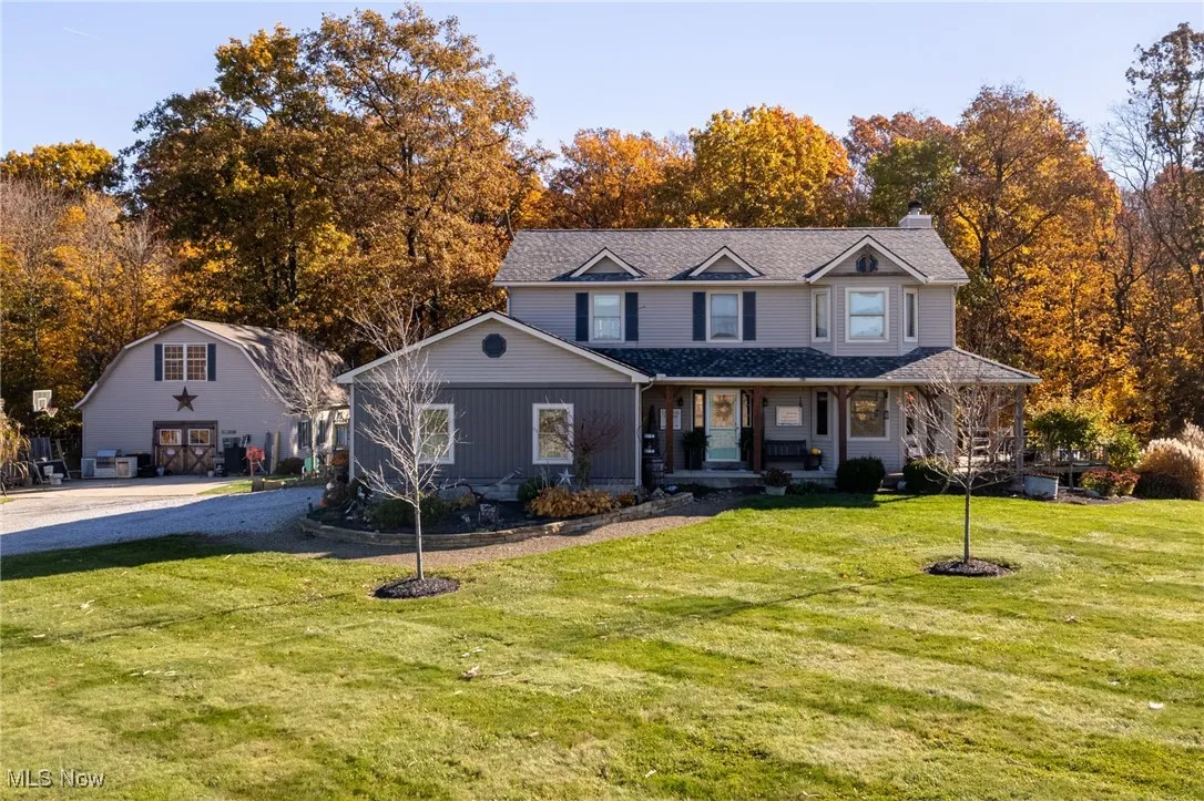 View of front of property with a porch, a front lawn, a chimney, and view of wooded area