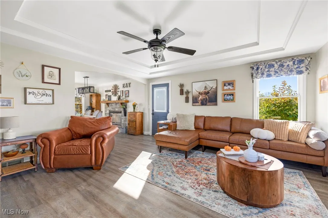 Living room with a tray ceiling, wood finished floors, ceiling fan, and a fireplace