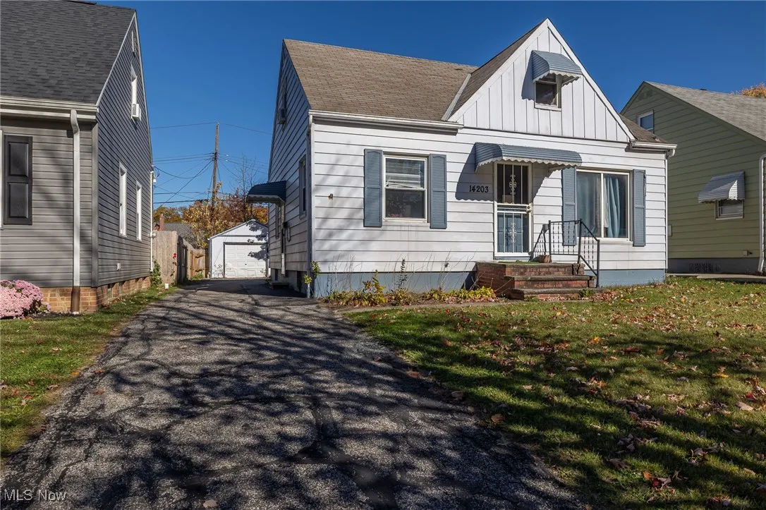 View of front of house with board and batten siding, a front yard, an outdoor structure, a detached garage, and roof with shingles
