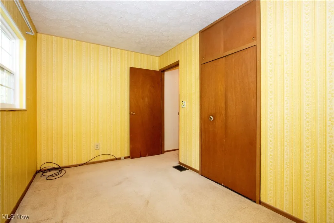 Unfurnished bedroom featuring wallpapered walls, a closet, carpet, and a textured ceiling