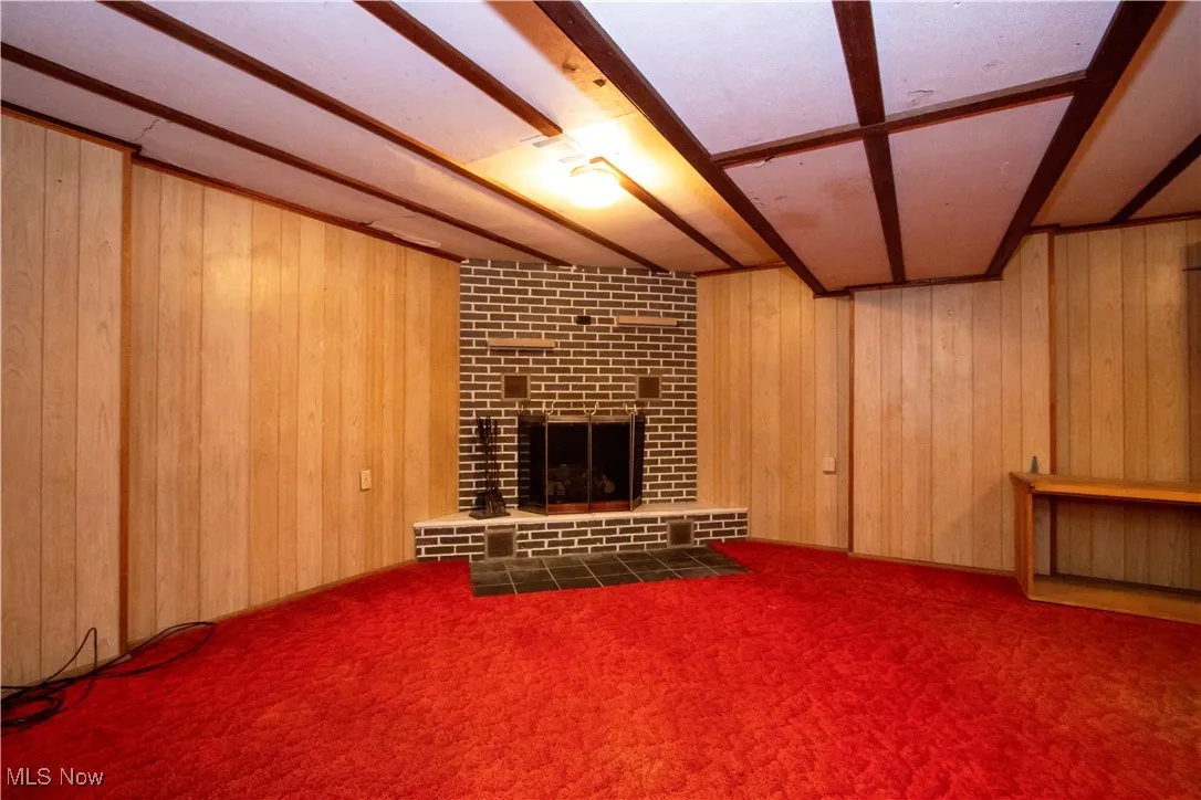 Unfurnished living room featuring wooden walls, a fireplace, and carpet