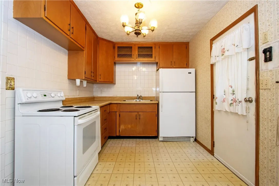 Kitchen featuring white appliances, light countertops, light floors, a chandelier, and wallpapered walls