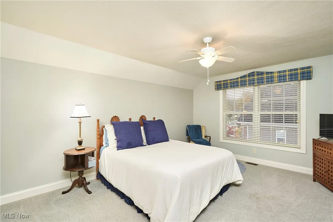 Bedroom with light colored carpet, lofted ceiling, ceiling fan, and a textured ceiling