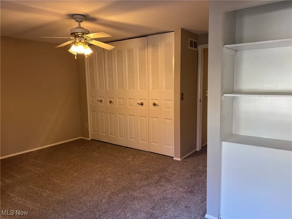 Unfurnished bedroom featuring double closet, built-in shelving, and a ceiling fan