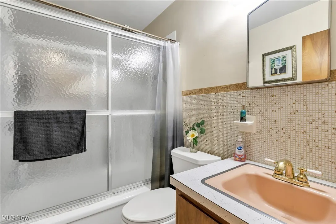 Full bath featuring bath / shower combo with glass door, tile walls, vanity, and a wainscoted​​‌​​​​‌​​‌‌​‌‌​​​‌‌​‌​‌​‌​​​‌​​ wall