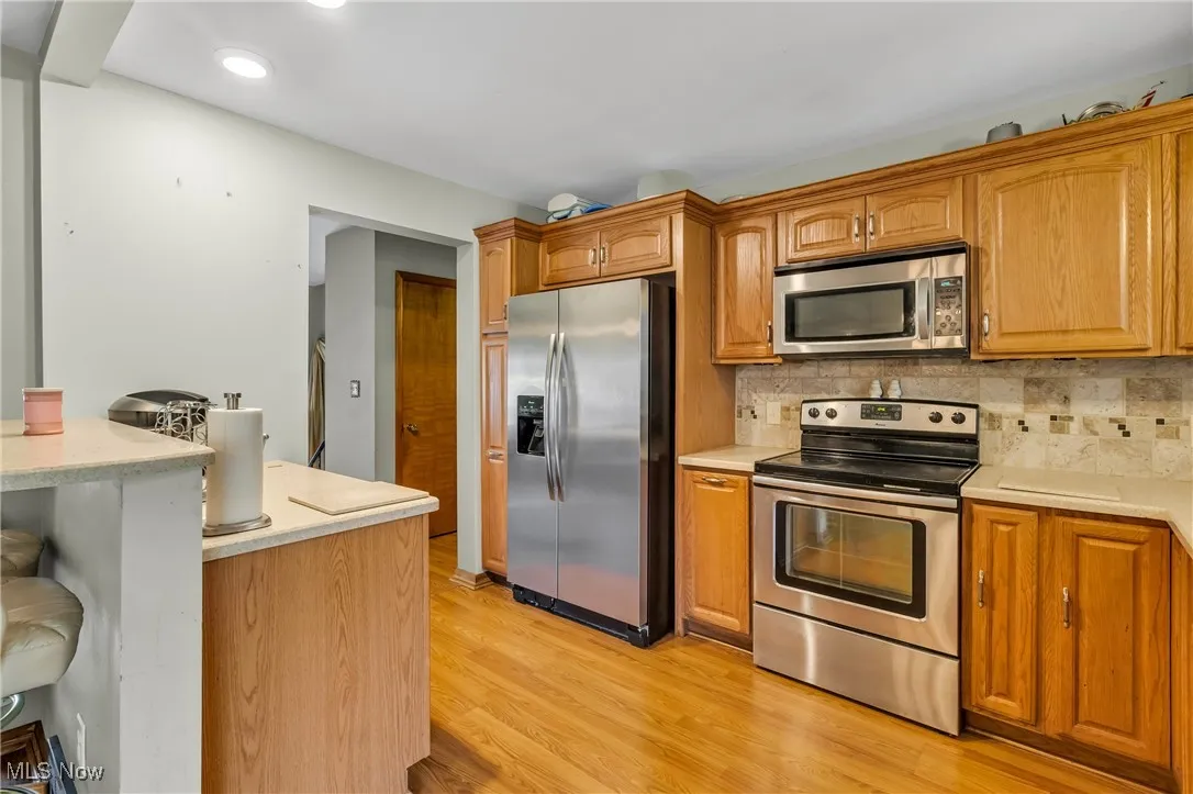 Kitchen featuring appliances with stainless steel finishes, a kitchen breakfast bar, backsplash, light wood finished floors, and brown cabinets