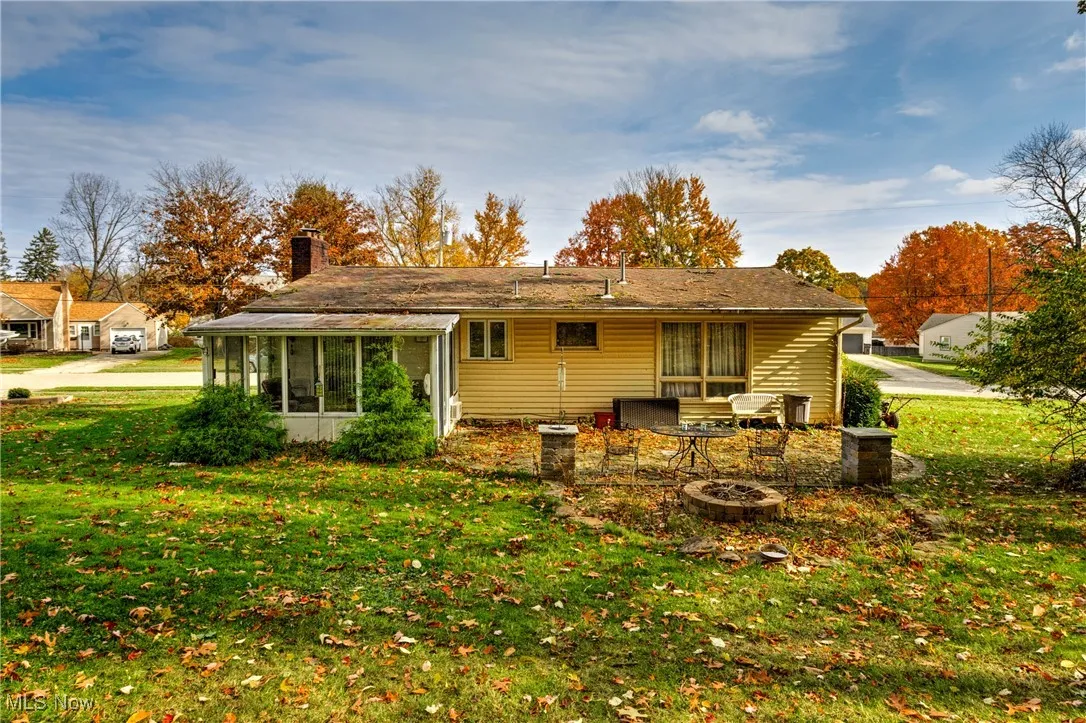 Rear view of property featuring an outdoor fire pit, a lawn, a sunroom, and a chimney