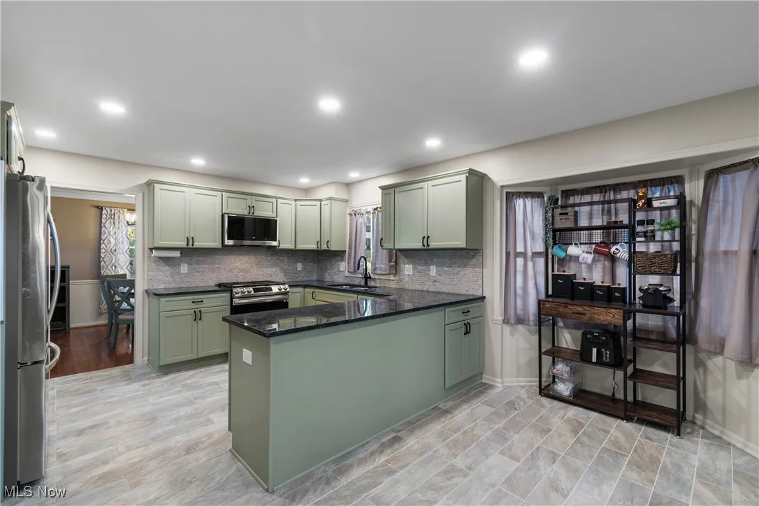 Kitchen with green cabinetry, dark stone countertops, stainless steel appliances, decorative backsplash, and a peninsula