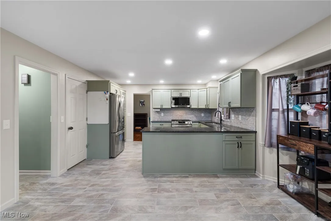 Kitchen with dark stone counters, tasteful backsplash, appliances with stainless steel finishes, a peninsula, and recessed lighting