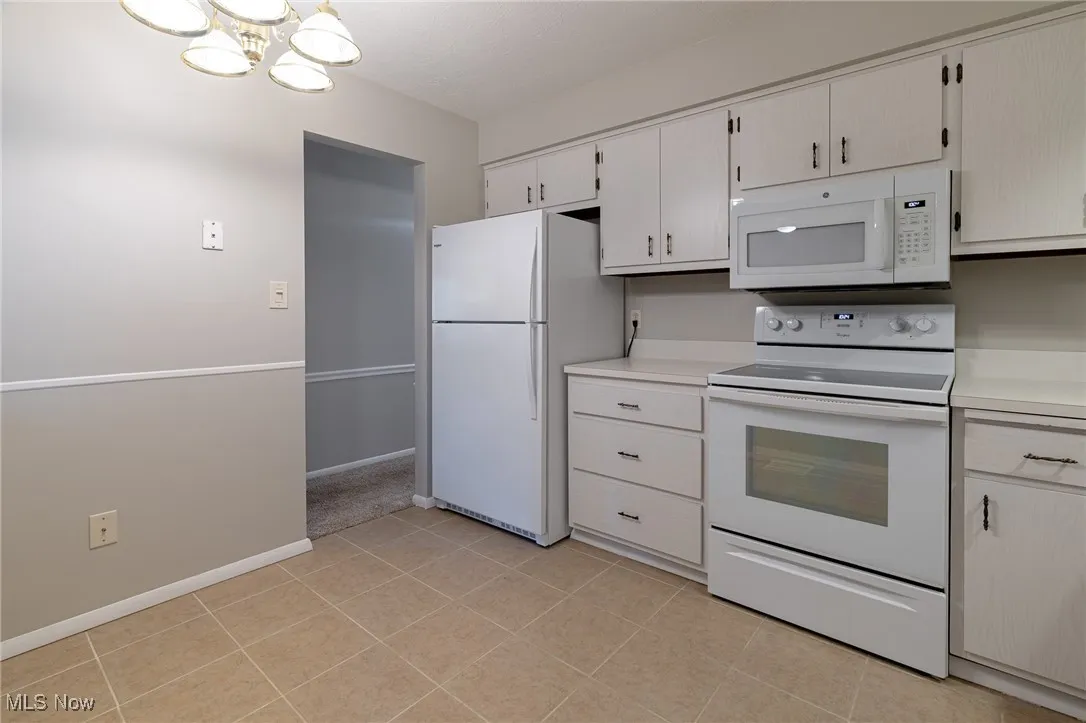 Kitchen with white appliances, light countertops, a chandelier, and light tile patterned flooring