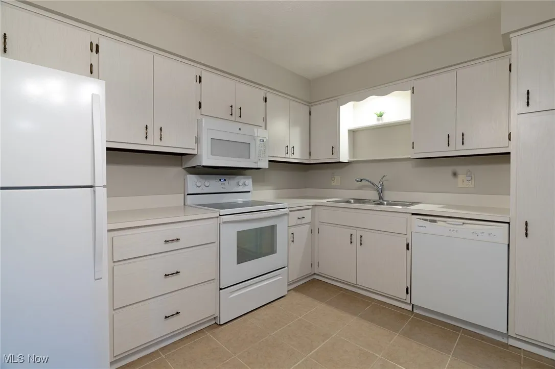 Kitchen featuring white appliances, light countertops, light tile patterned floors, and white cabinetry