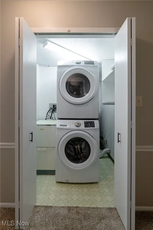 Laundry room with stacked washer and clothes dryer and light colored carpet