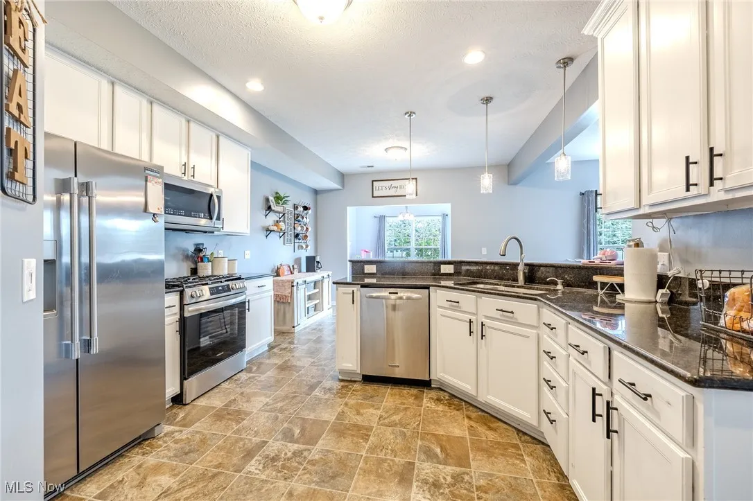 Kitchen featuring appliances with stainless steel finishes, white cabinets, a peninsula, decorative light fixtures, and dark stone counters